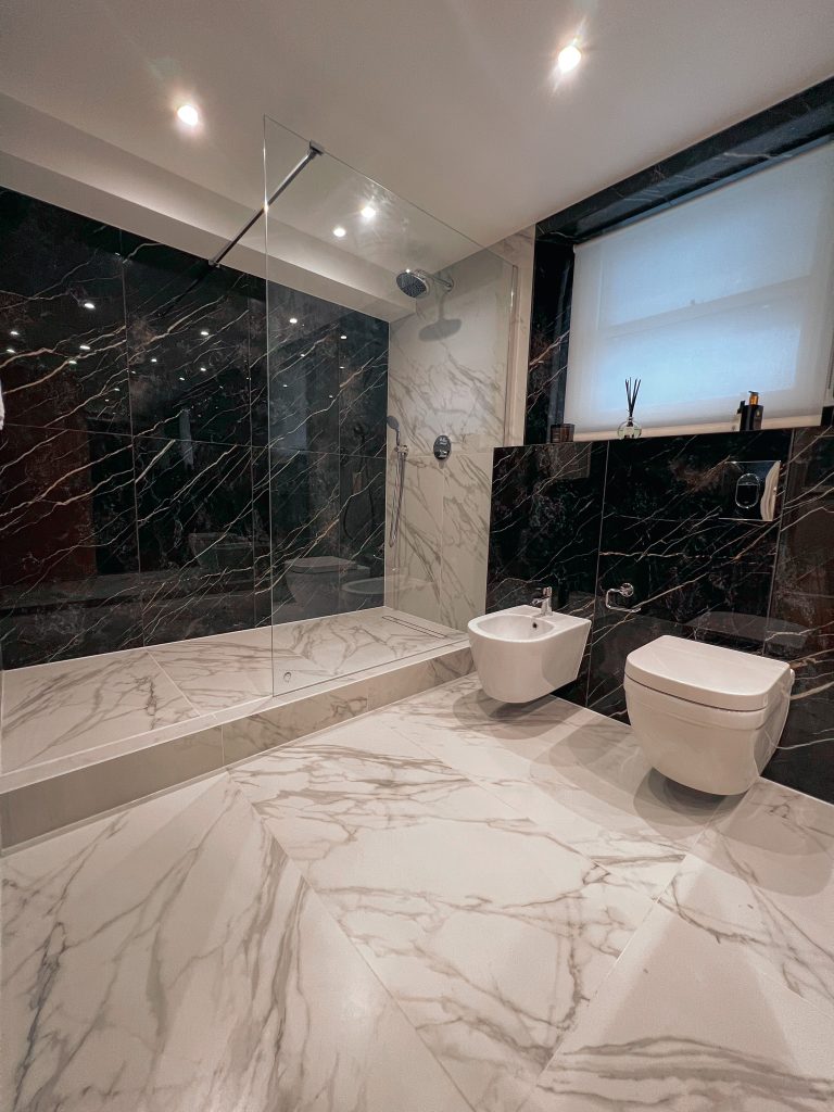 A modern bathroom with marble tiles, a glass shower enclosure, and white sanitary fixtures.